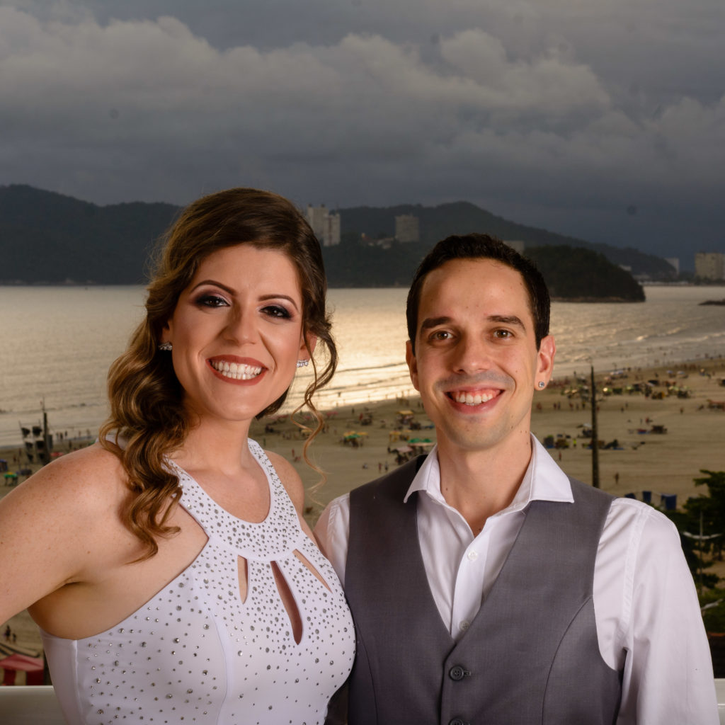casal de noivos posam em uma sacada com a ilha Urubuqueçaba ao fundo num por do sol em Santos.