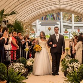 fotografia de casamento de uma noiva com seu pai entrando no corredor durante a cerimonia. convidados observam, fotografam e filmam com sues celulares.